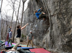 A person boulding on a rock while others are spotting him.