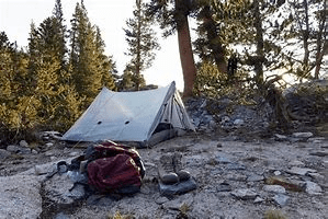 A tan tent set up in a rocky clearing.